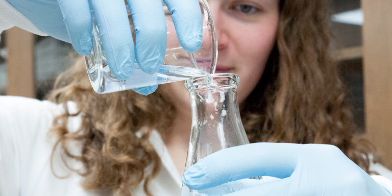 A close-up photo of a girl pouring a liquid into a beaker